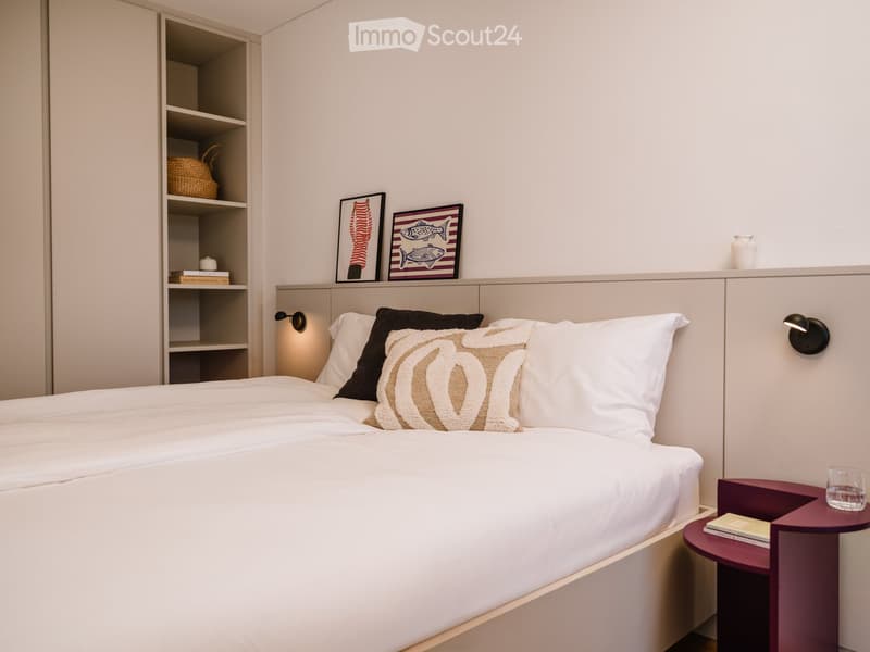 Modern bedroom with a neatly made bed, nightstand, and decorative items on shelves and walls.