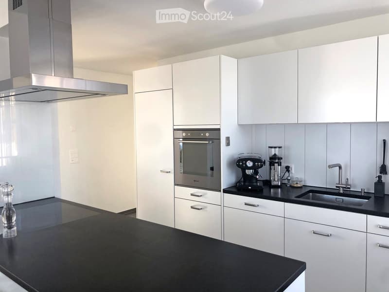 Modern kitchen with white cabinets, black countertops, stainless steel appliances, and a coffee station.