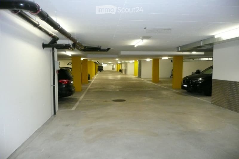 Underground parking garage with concrete floors, yellow support pillars, and several parked cars.