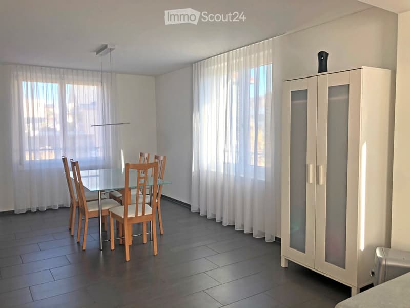 Modern dining room with a glass dining table, wooden chairs, and a white cabinet with glass doors.