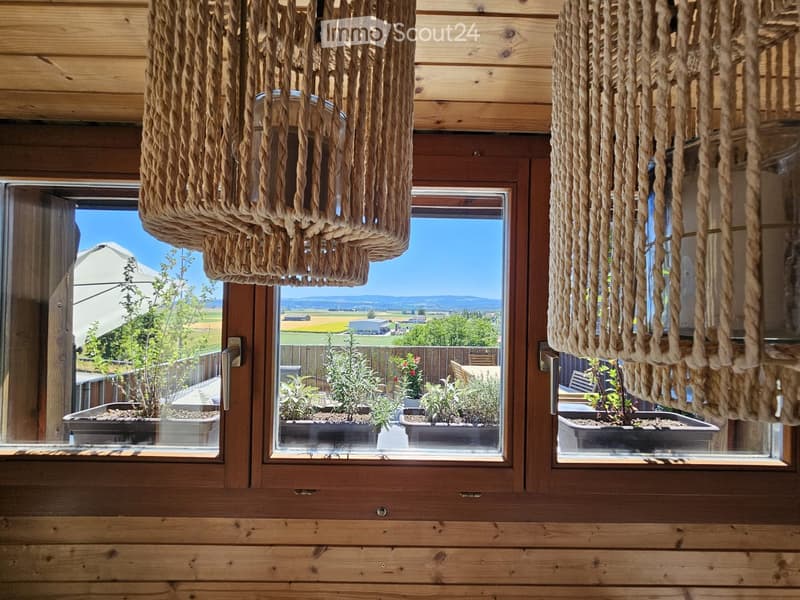 Wooden balcony with large windows, hanging rope light fixtures, and potted plants visible outside.