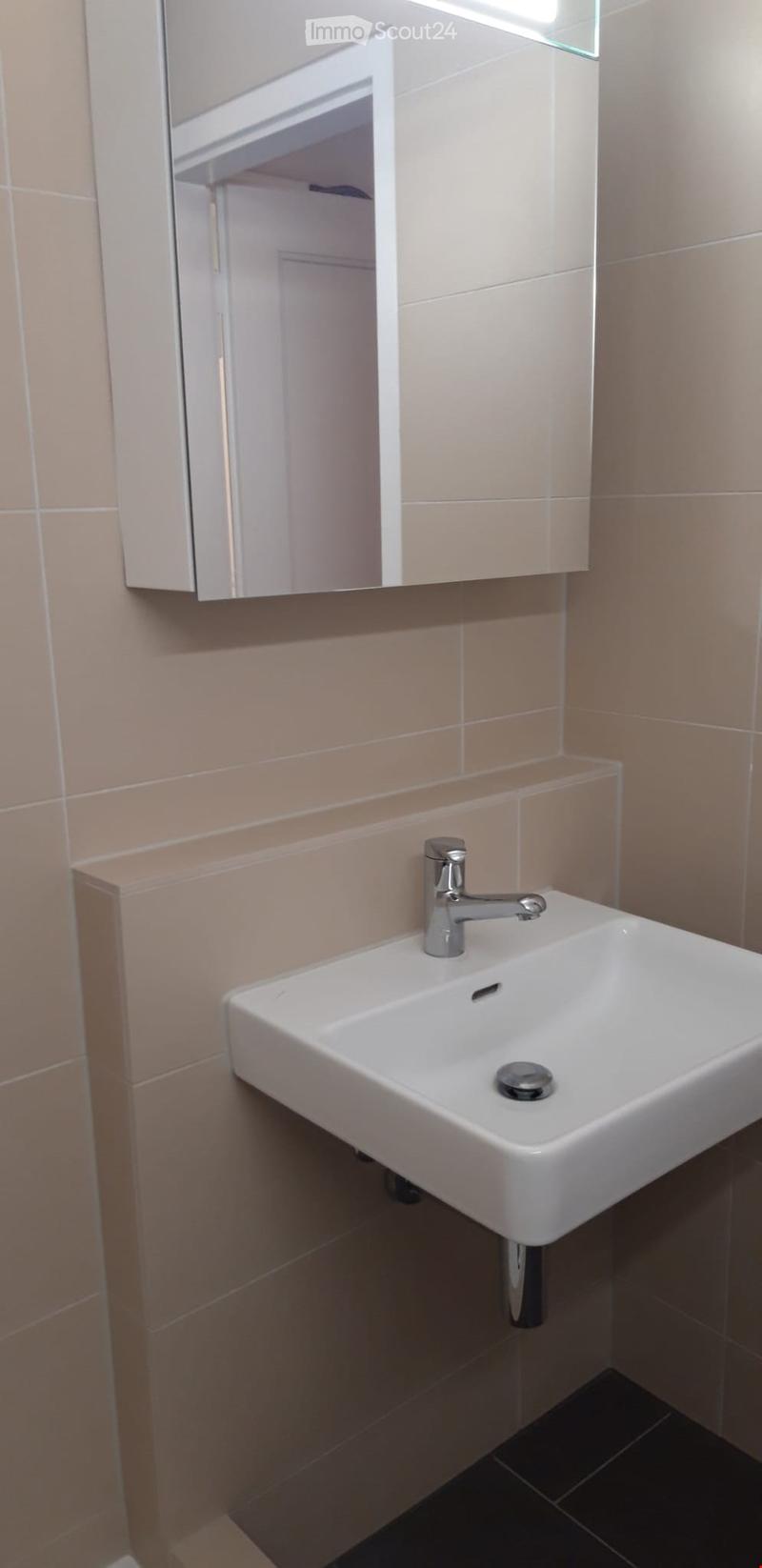 Modern bathroom with a white sink, chrome faucet, and a mirrored cabinet above it. Beige tiled walls and dark tiled floor.