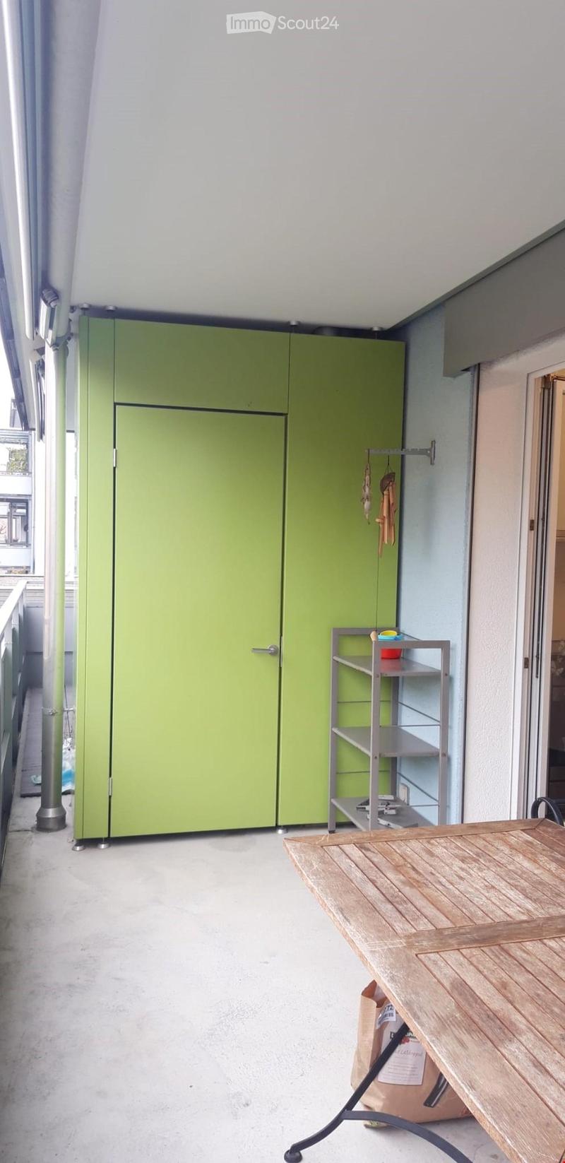 Balcony with a green cabinet, a wooden table, a metal shelf, and a hanging coat rack.