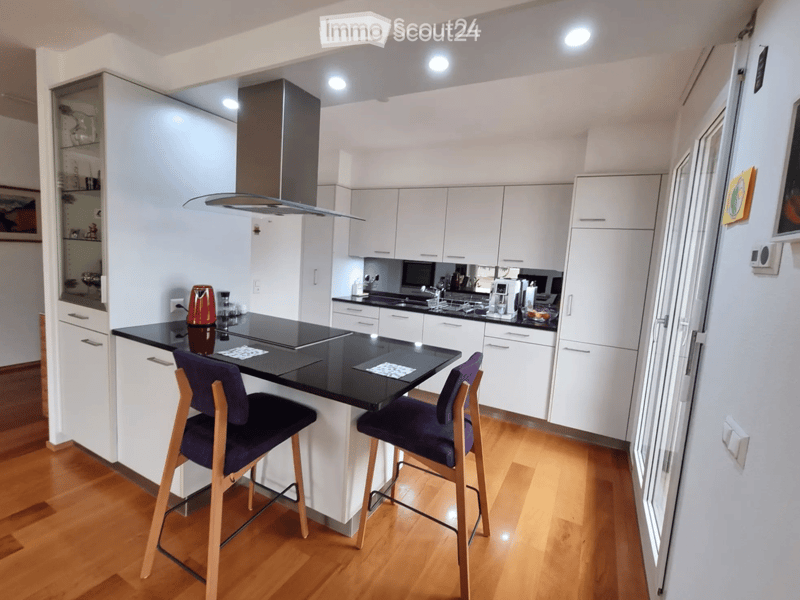Modern kitchen with white cabinets, black countertop, wooden floor, and two bar stools.