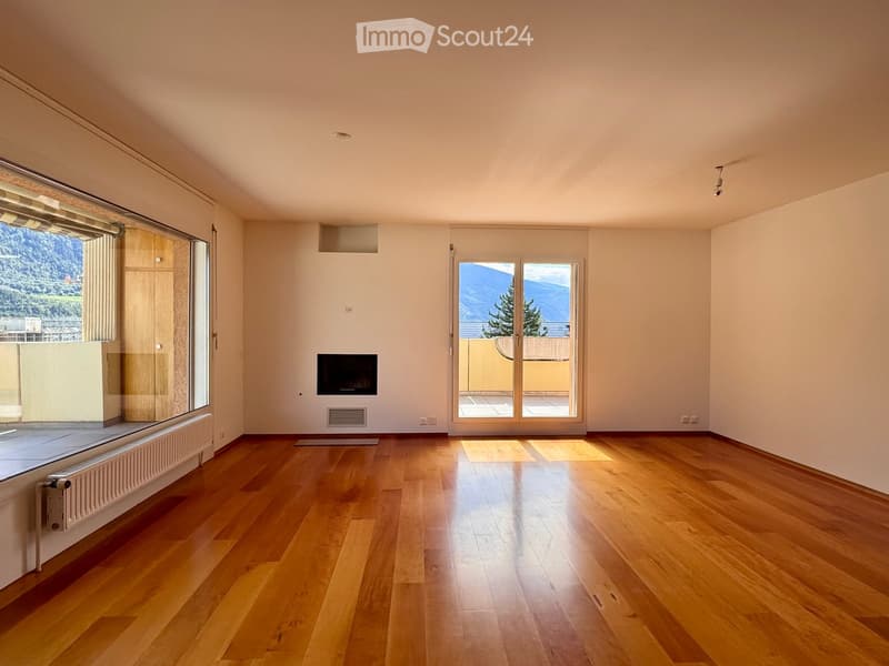 Empty room with wooden flooring, large windows, and a fireplace, featuring a view of the mountains.