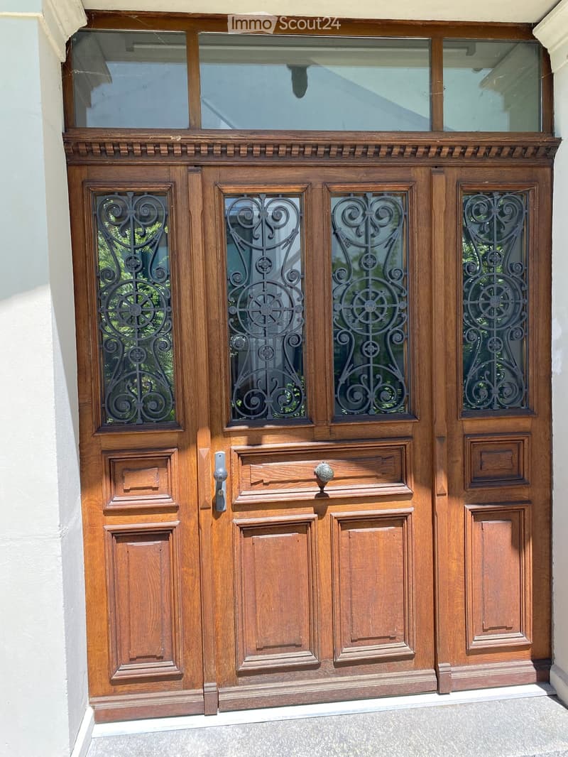 Wooden double front door with ornate metalwork and glass panels, featuring decorative carvings and a transom window above.