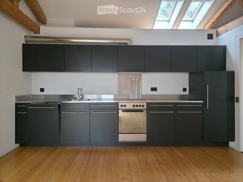Modern kitchen with dark grey cabinets, stainless steel appliances, and wooden flooring.