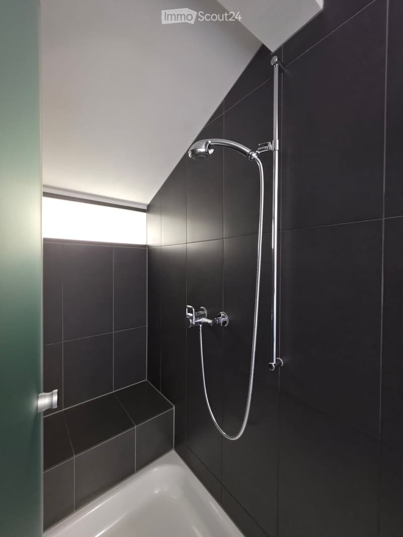 Modern bathroom with black tiled walls, a white bathtub, and a sleek showerhead with handheld sprayer.