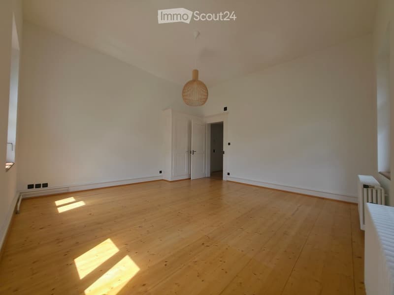 Empty room with wooden flooring, white walls, and a hanging pendant light. There are two white doors leading to other spaces.