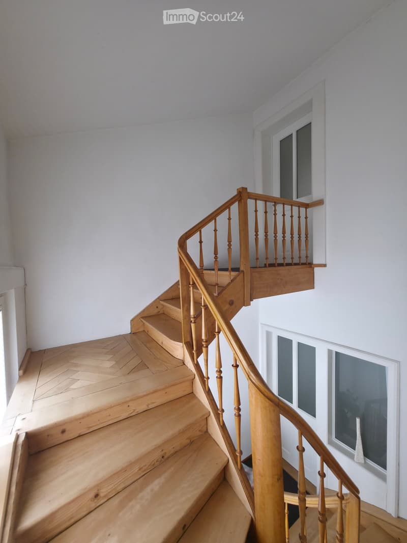 Spiral staircase with wooden steps and handrail, white walls, and large windows.