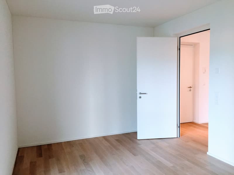 Empty room with light wooden flooring and white walls, featuring a closed white door leading to another room.