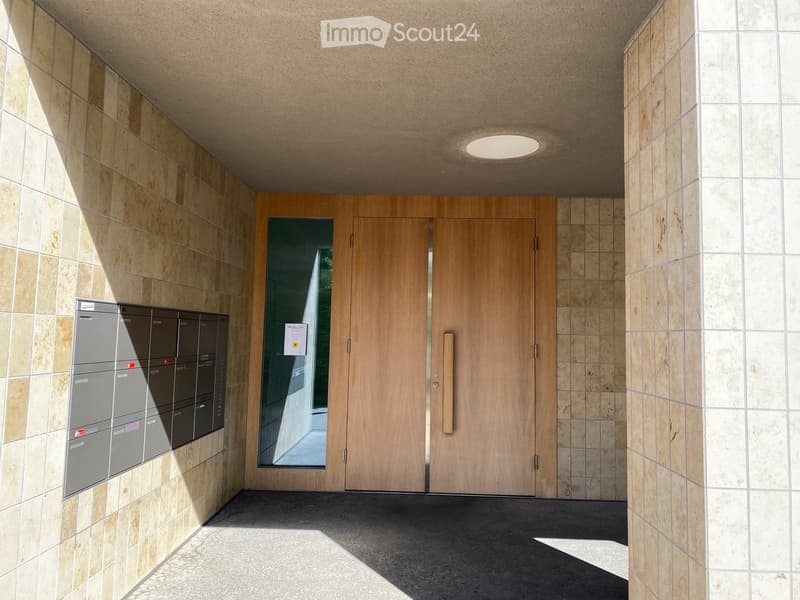 Modern hallway with tiled walls, wooden double doors, and mailboxes on the left side.