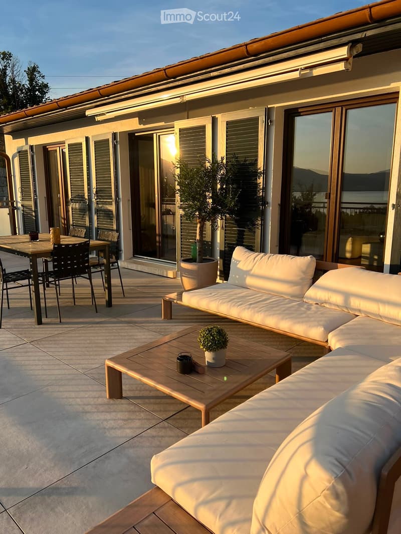 Terrace with a sofa, coffee table, dining table, and chairs, overlooking a scenic view.