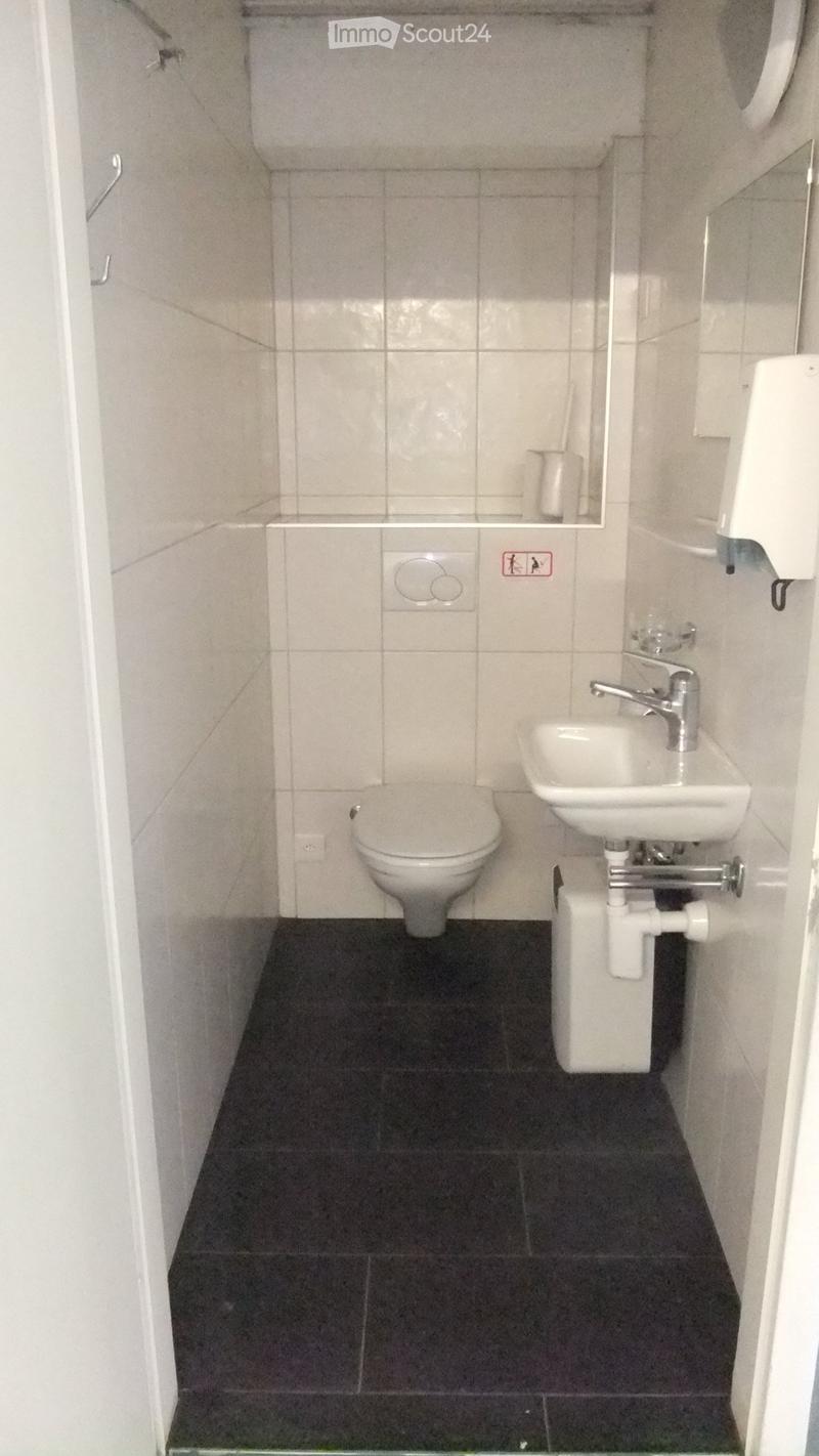 Small bathroom with white tiled walls, dark tiled floor, toilet, sink with chrome faucet, and a mirror above the sink.