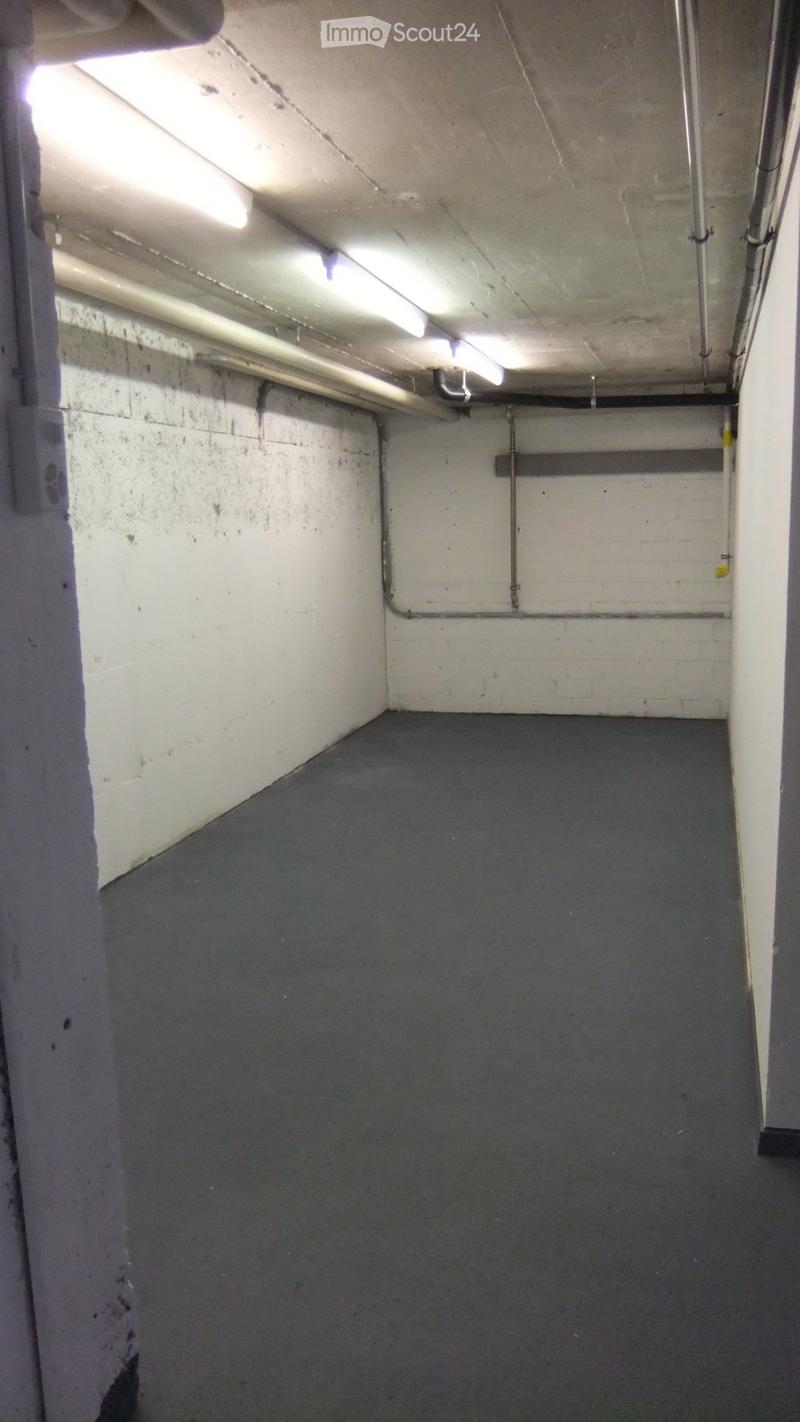 Empty room with concrete walls, a dark grey floor, and exposed pipes and lighting fixtures on the ceiling.