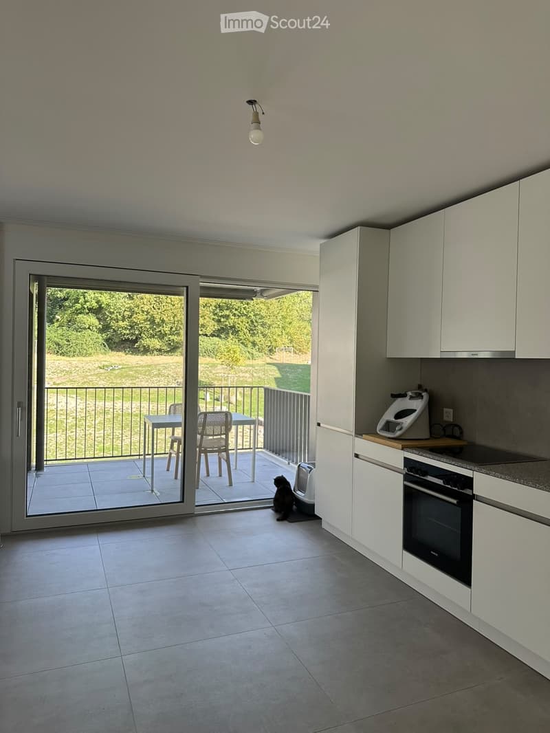 Modern kitchen with white cabinets, tiled floor, and a sliding glass door leading to a balcony with outdoor furniture.