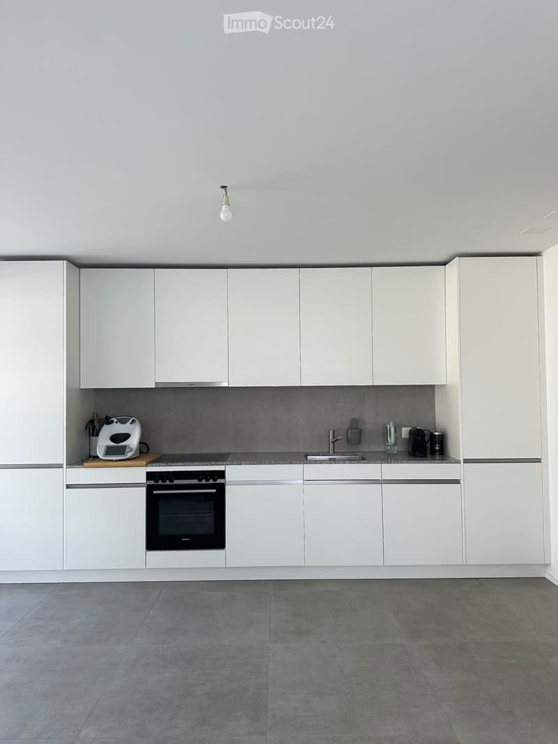 Modern kitchen with white cabinets, grey tiled backsplash, and grey tiled floor. Features an oven, toaster, and sink with a faucet.