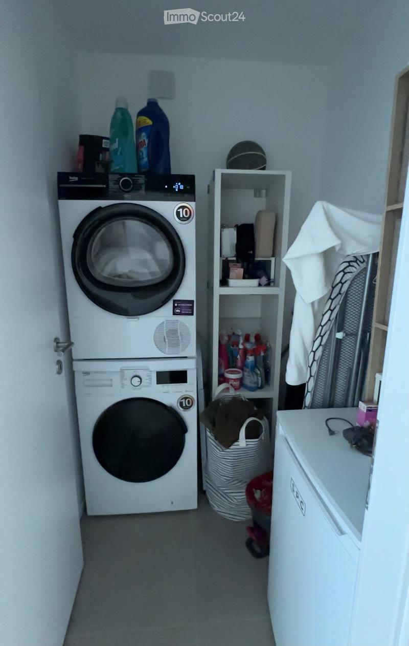 A small laundry area with a stacked washing machine and dryer, a shelf with cleaning supplies, and a basket on the floor.