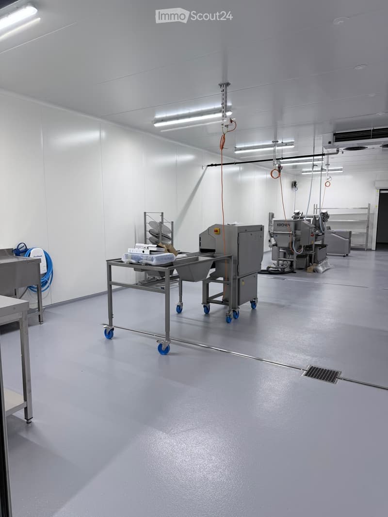 Clean, industrial-style room with stainless steel equipment, a sink, and a table with wheels. The space is well-lit with white walls and a smooth gray floor.