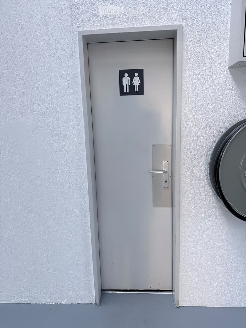 A closed grey restroom door with a male and female symbol sign, mounted on a white textured wall.