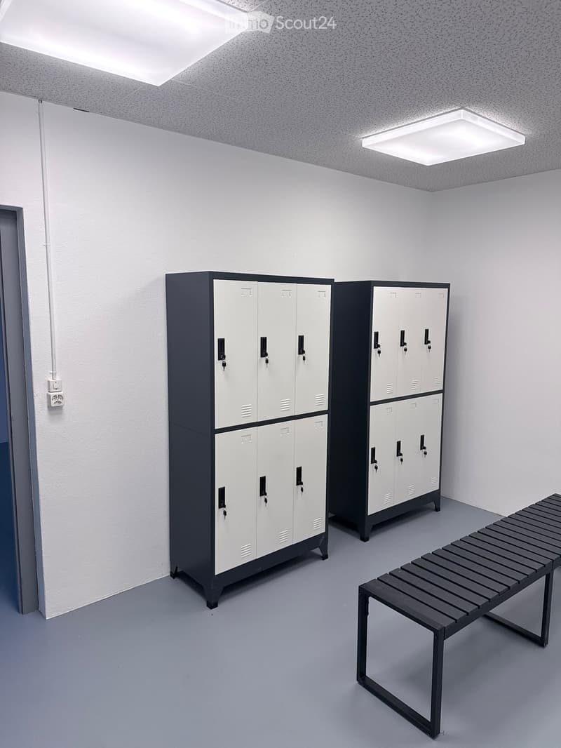 A clean, modern locker room with white and black lockers, a bench, and bright overhead lighting.
