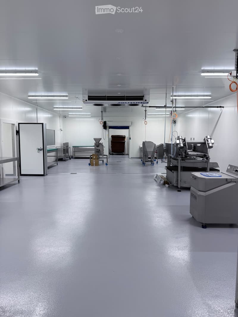 Clean, well-lit industrial room with stainless steel equipment, tables, and a large door leading to another area.