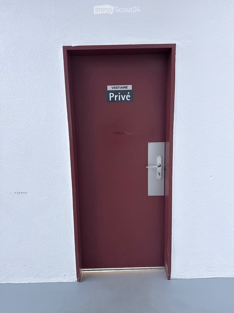A maroon door with a silver handle and a sign reading "Privé" in a hallway with white walls and a grey floor.