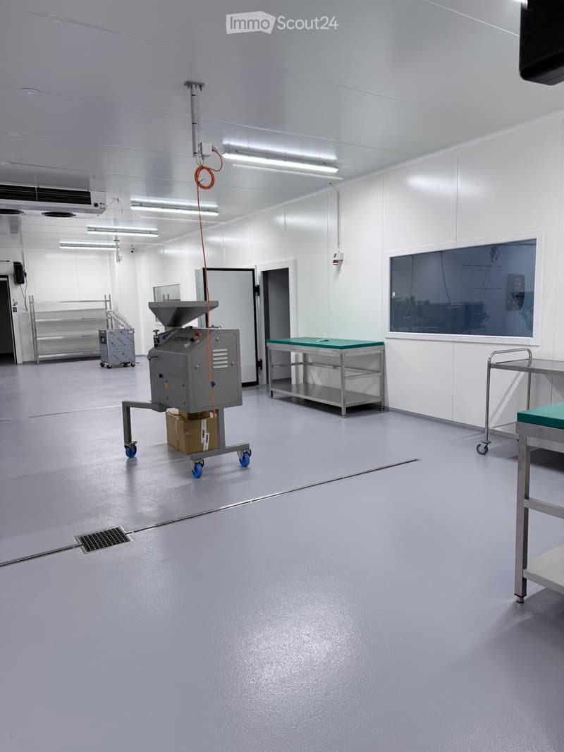 Clean, well-lit industrial room with a grey floor, white walls, and various equipment including a table, a machine on wheels, and a cart.