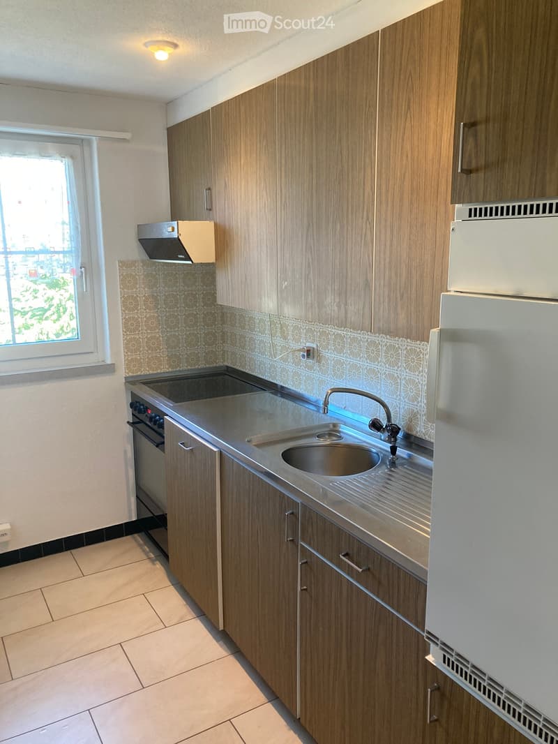 Modern kitchen with wooden cabinets, stainless steel sink, faucet, oven, and refrigerator. Features a window with a view and patterned backsplash tiles.