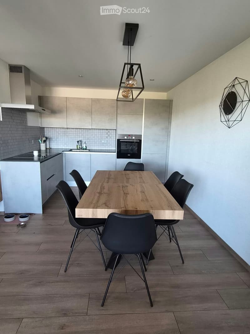 Modern kitchen and dining area with light grey cabinets, a wooden dining table, black chairs, and a pendant light fixture.