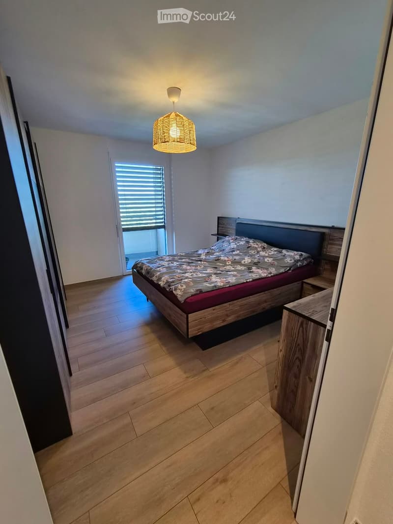 Modern bedroom with wooden flooring, a large bed with a dark headboard, a pendant light fixture, and a nightstand.
