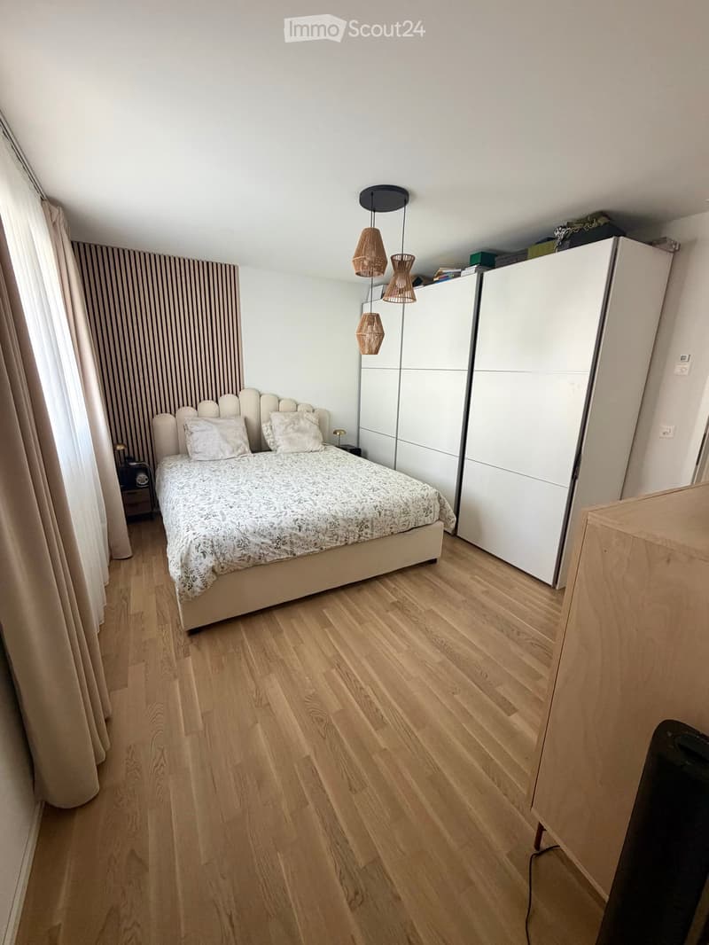 Modern bedroom with a large bed, white bedding, wooden floor, white wardrobe, and pendant lights.