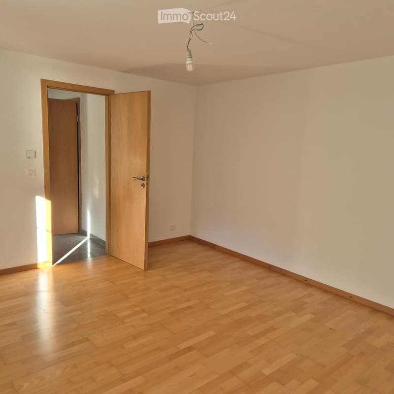Empty room with wooden flooring, white walls, and a single open wooden door leading to another space.
