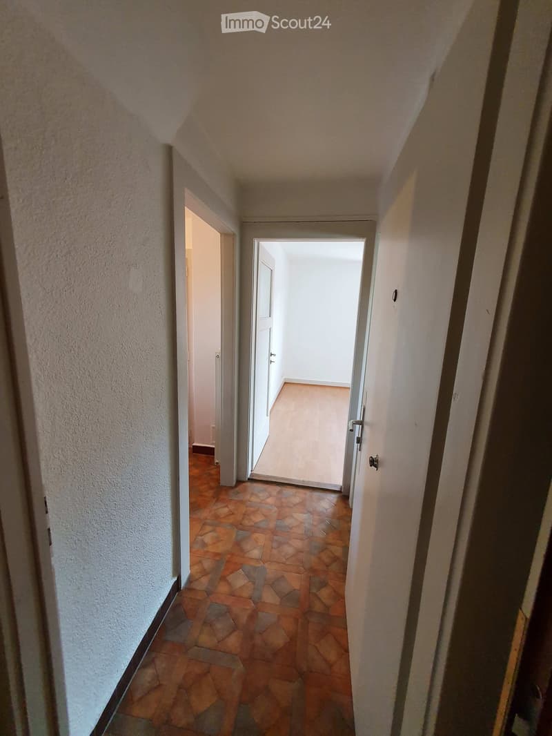 A narrow hallway with tiled flooring and white walls, featuring two open doors leading to adjacent rooms.