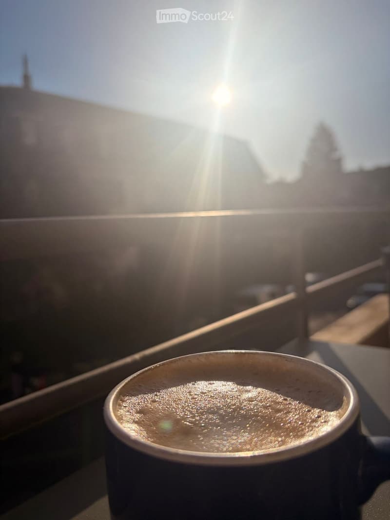 A cup of coffee sits on a table with a view of the city and the sun shining brightly in the background.