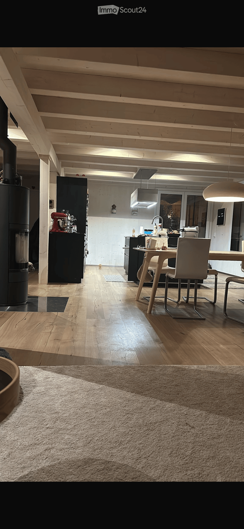 Open-plan kitchen and dining area with wooden flooring, modern pendant lighting, and contemporary furniture including a dining table and chairs.