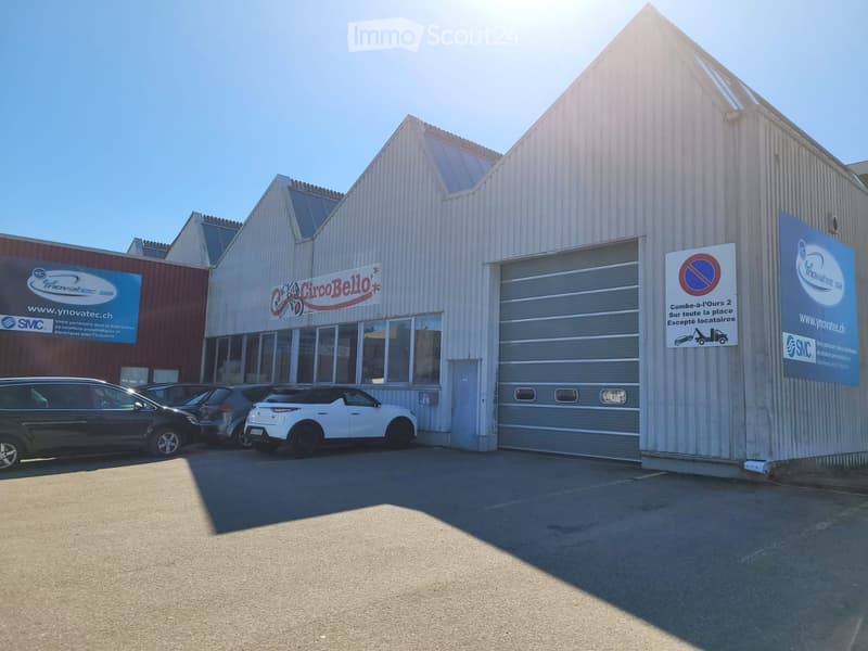 Commercial building with large garage, metal siding, visible parking area, large windows, brand name signs