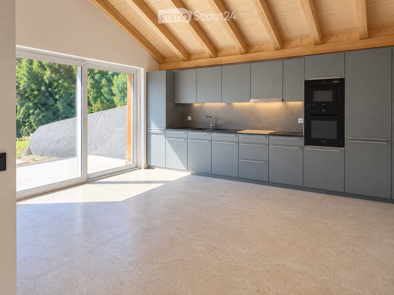 Modern kitchen with grey cabinets, stainless steel appliances, and a large window overlooking a garden.
