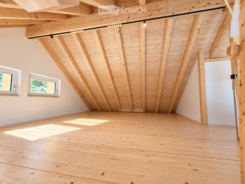 Empty attic space with exposed wooden beams, wooden flooring, and two windows letting in natural light.