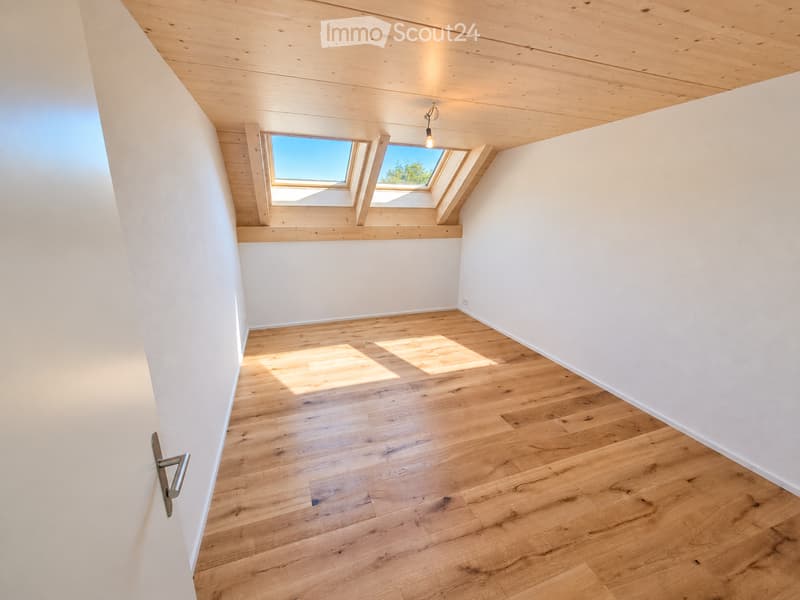 Bright, empty room with wooden flooring and white walls, featuring a skylight window and a single light fixture on the ceiling.