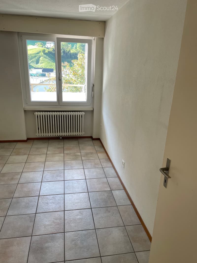 Empty room with tiled floor, white walls, a radiator, and a large window with a view of greenery.