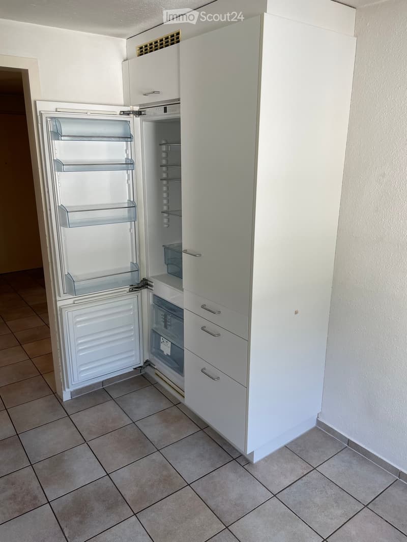 Modern kitchen with white cabinets and a stainless steel refrigerator. The refrigerator is open, showing its interior compartments.