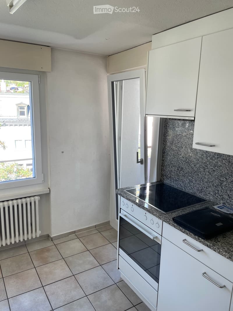 Modern kitchen with white cabinets, granite countertop, induction stove, and oven. Features tiled floor and radiator.