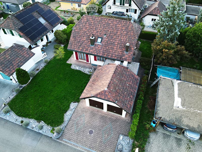 Aerial view of a residential area with multiple houses, featuring tiled roofs, solar panels, garages, and well-maintained gardens.