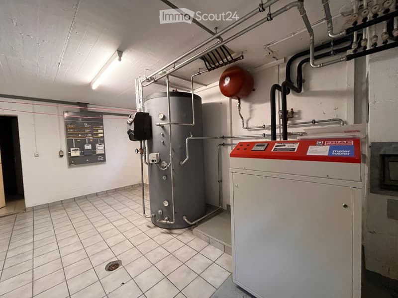 Utility room with a large water tank, a boiler, and a control panel mounted on the wall.