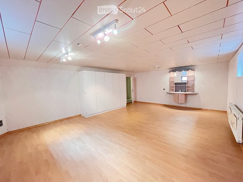 Empty room with light wooden flooring, white walls, built-in cabinets, and a small kitchenette area with a sink and countertop.