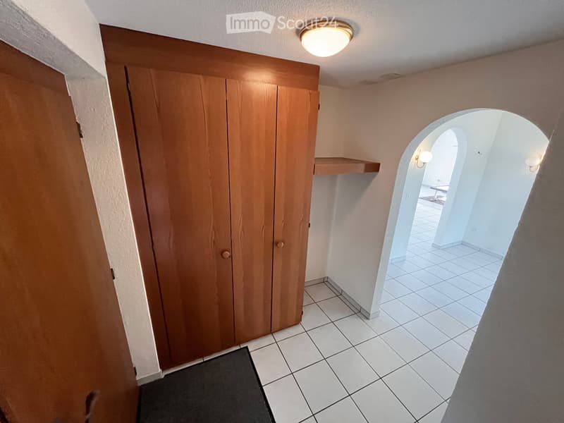 Empty hallway with tiled flooring, wooden closet, arched doorway leading to another room, and a small shelf.