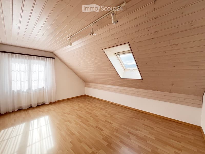 Empty attic room with wooden walls, wooden floor, skylight window, and white curtains on one wall.