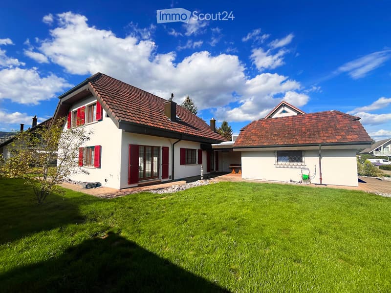 Two-story house with red-tiled roof, white walls, red shutters, and a well-maintained lawn.