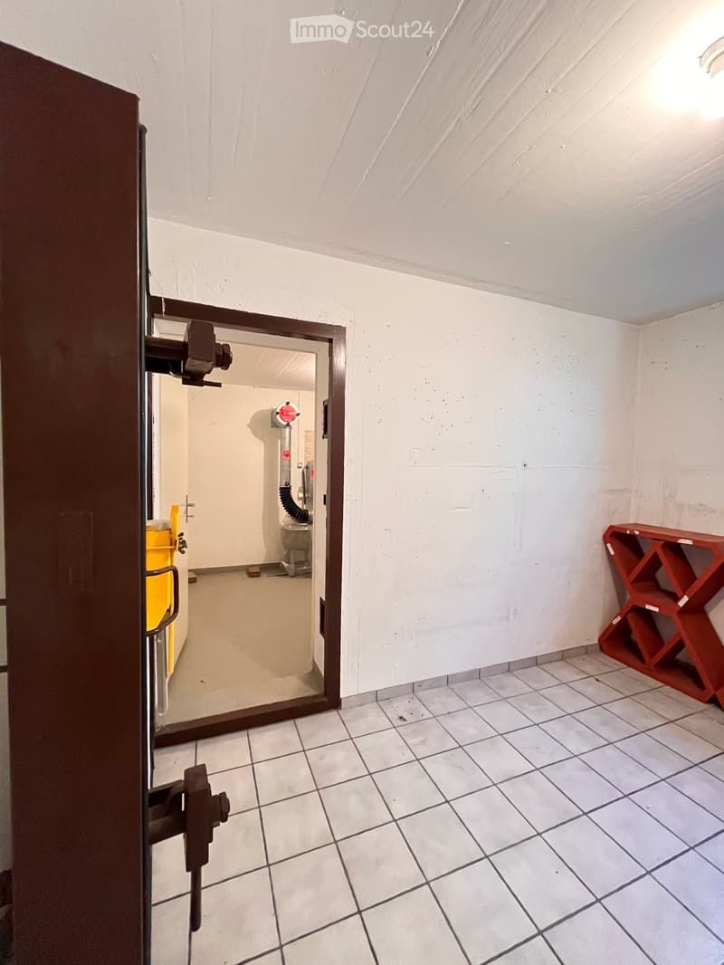 Empty room with tiled floor, white walls, and a partially open door leading to another room. A red shelving unit is visible in the corner.